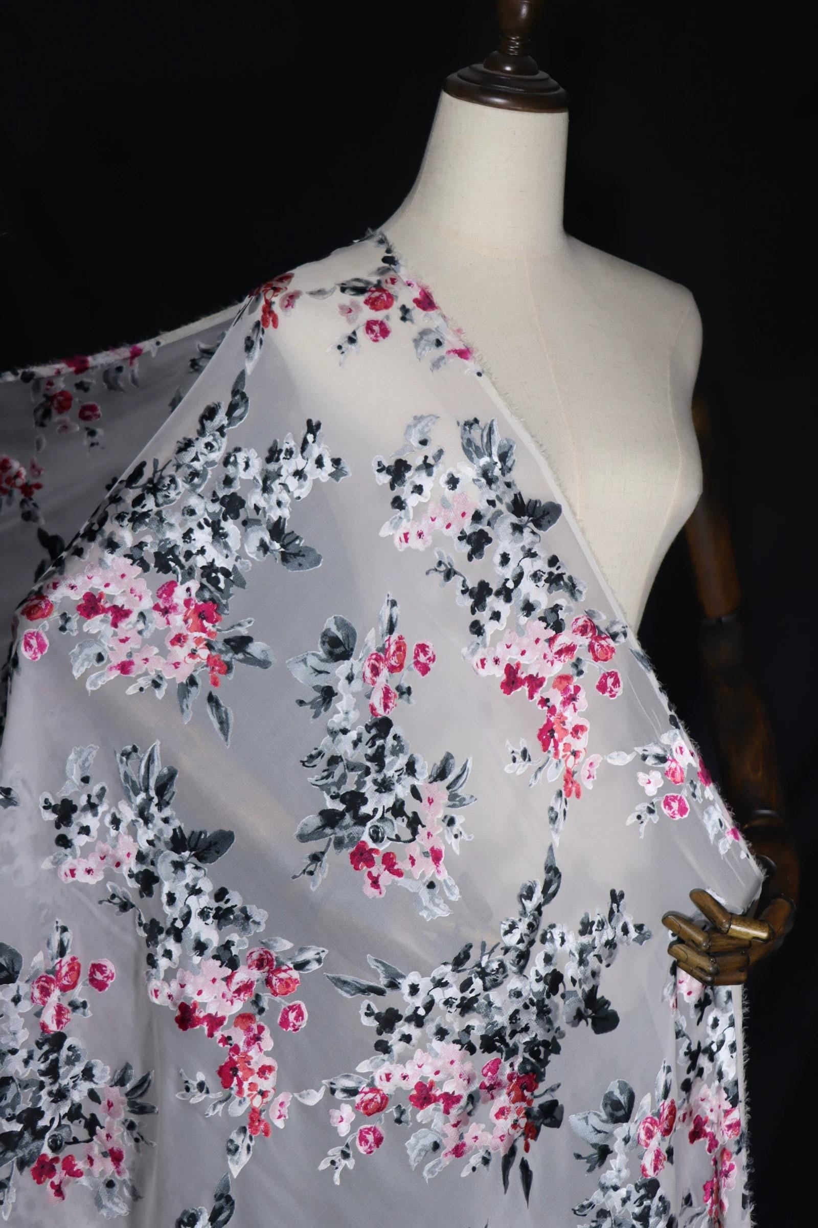 A mannequin wearing a white dress with a floral print, featuring a mix of pink, black, and white flowers.