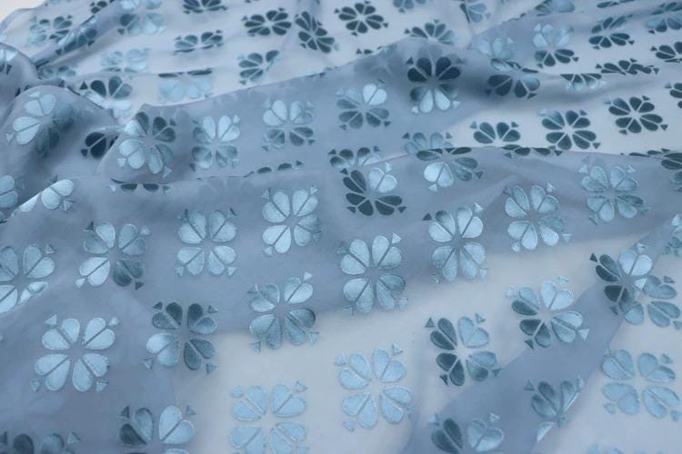 a close-up view of a fabric with a repeating pattern of blue and white flower-like designs.