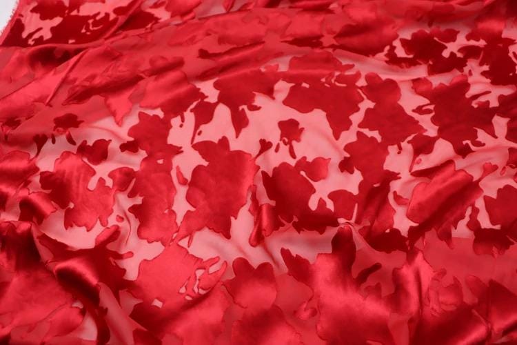 a close-up view of a red fabric with a floral pattern, featuring a repeating design of red flowers or leaves.