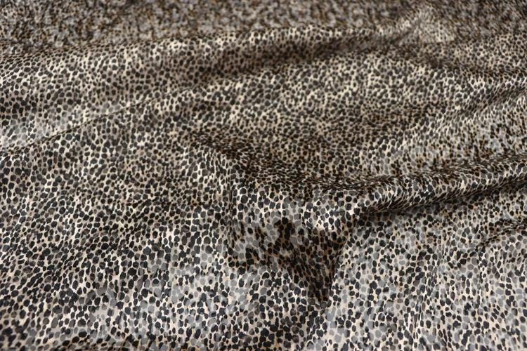 a close-up view of a fabric with a distinctive leopard print pattern. The fabric appears to be made of a material with a textured surface, resembling the appearance of a cat's fur. The pattern consists of small, irregularly shaped dots or spots in various shades of brown and black, creating a visually striking and textured design.
