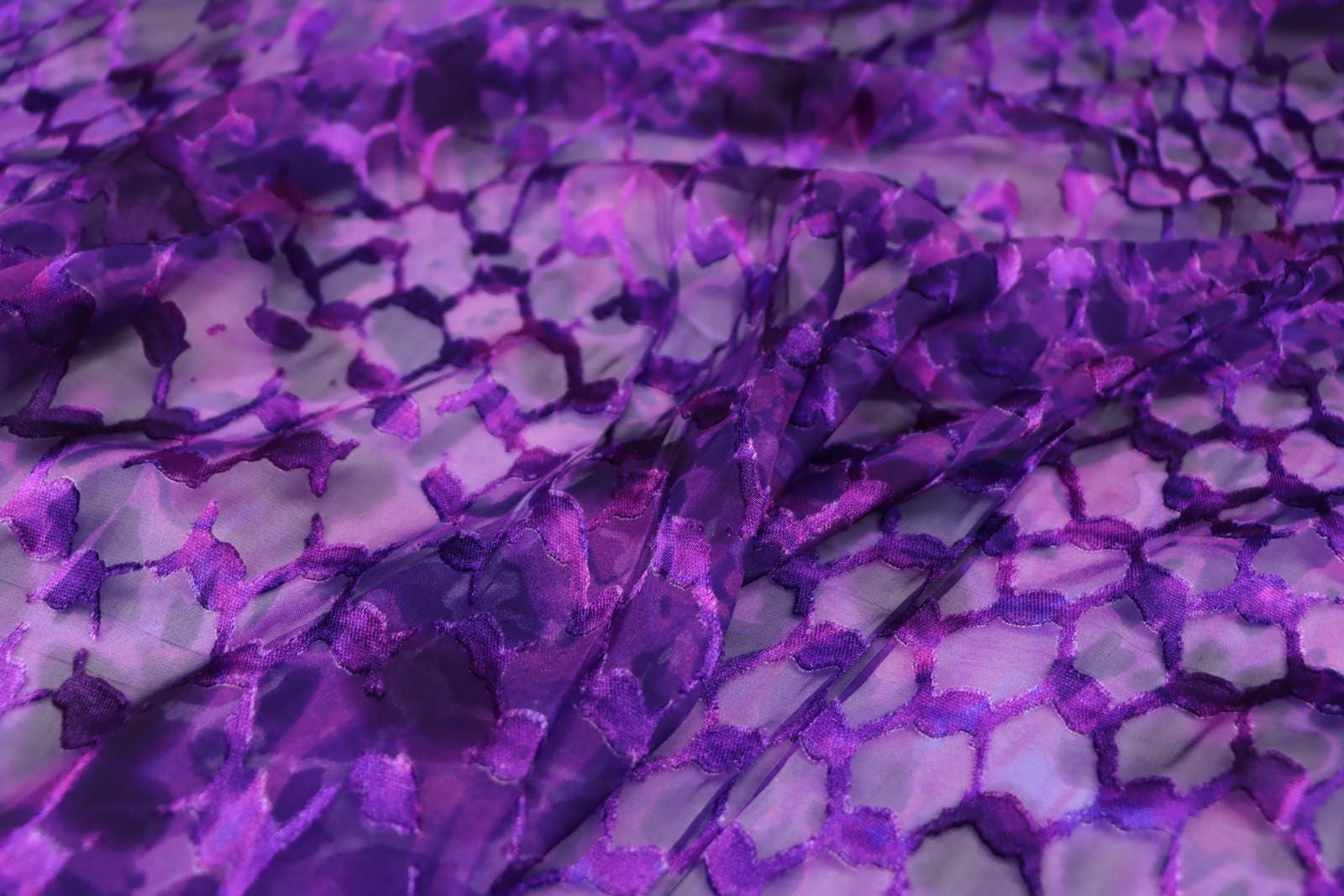 a close-up view of a fabric with a purple and white pattern, featuring a repeating hexagonal design.