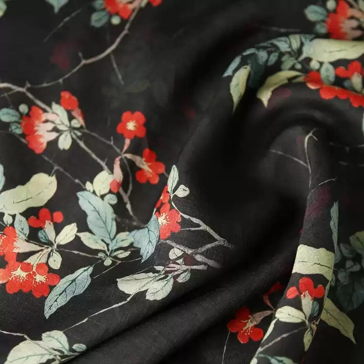 a close-up view of a fabric with a floral pattern in shades of black and red. The fabric appears to be made of silk or a similar material, and the pattern features red flowers and green leaves. The fabric is crumpled, giving it a textured appearance.