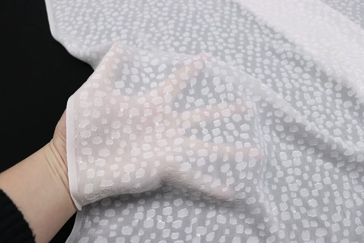 A hand is holding a piece of fabric with a white polka dot pattern.