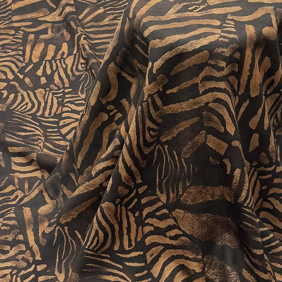 a close-up view of a fabric with a striking zebra-like pattern in shades of black and gold. The pattern is intricate and detailed, with the zebra's distinctive black and white stripes prominently displayed. The fabric appears to be made of a soft, plush material, and the zebra pattern adds a bold and eye-catching element to the overall design.