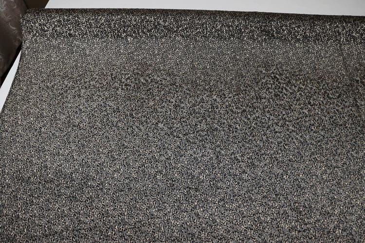 a close-up view of a textured surface, possibly a carpet or a piece of fabric, with a pattern of small black dots or specks covering the entire surface.