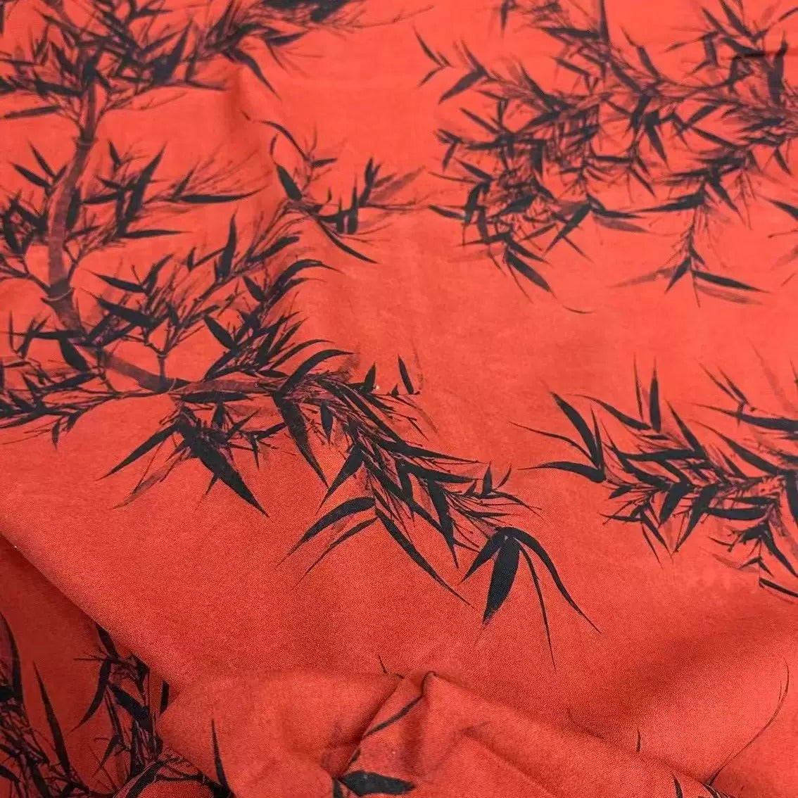 a close-up view of a fabric with a striking red background and black leaf-like patterns. The pattern appears to be a repeating design, creating a visually captivating and textured appearance.