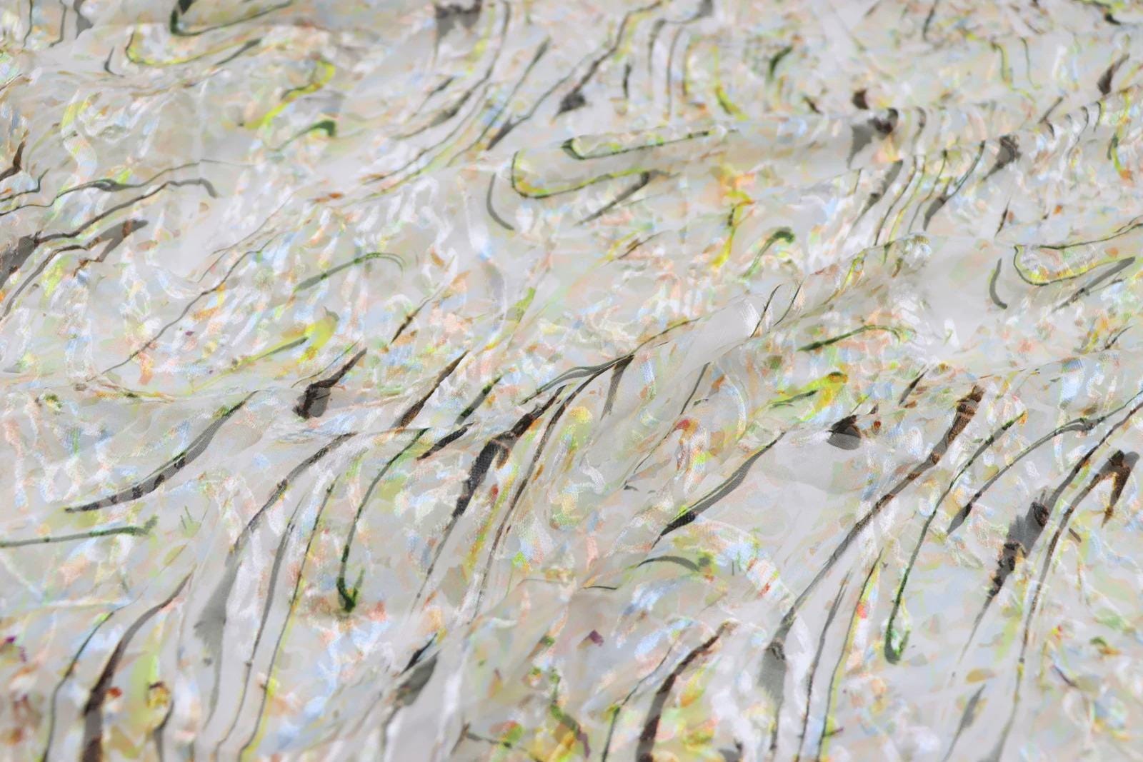 The image is a close-up of a fabric with a colorful, abstract pattern of lines and shapes in various shades of green, yellow, and orange.