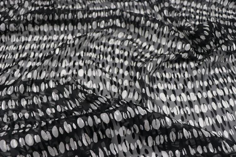 a close-up view of a fabric with a black and white polka dot pattern. The fabric appears to be made of a sheer material, with a crumpled texture that gives it a soft and flowing appearance.