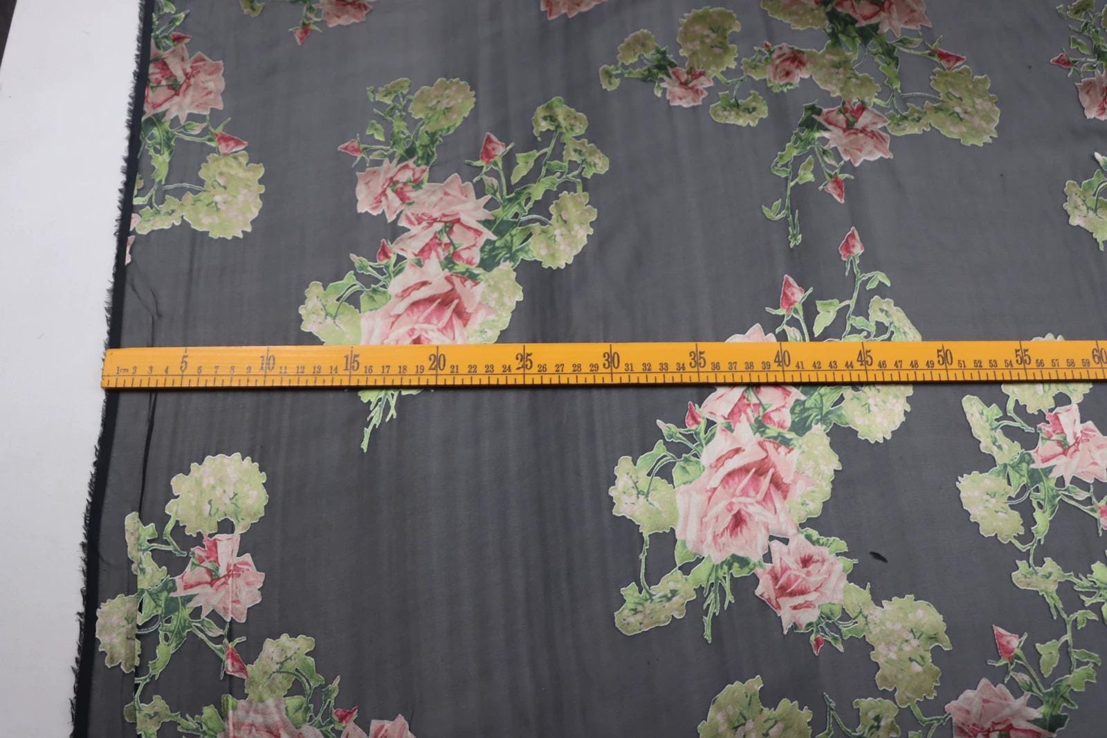 a close-up view of a fabric with a floral pattern, featuring a yellow measuring tape placed across it.