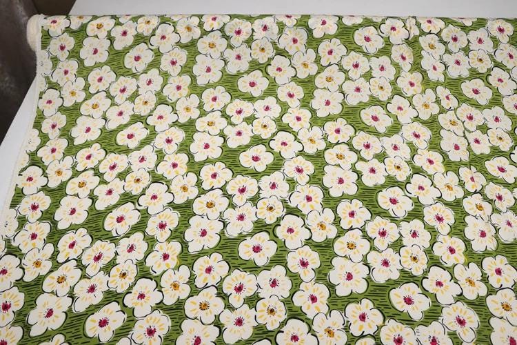 a close-up view of a fabric with a repeating pattern of white flowers on a green background.