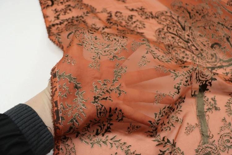 A close-up view of a hand holding a piece of fabric with a floral pattern in shades of orange and black.