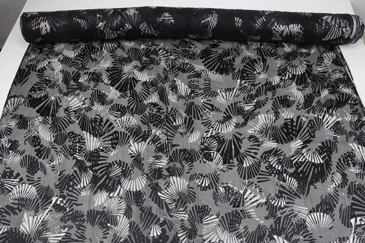 a black and white fabric with a repeating pattern of black and white fan-like shapes. The fabric appears to be rolled up and displayed on a surface.
