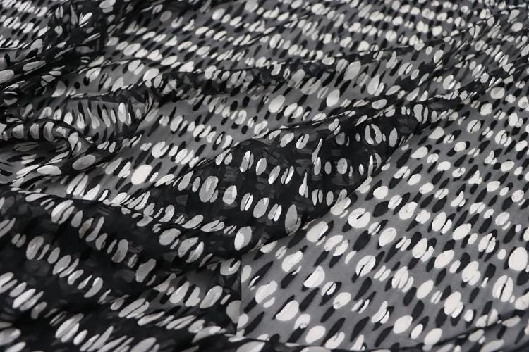 a close-up view of a fabric with a black and white polka dot pattern. The fabric appears to be made of a sheer material, with a textured and wrinkled appearance.
