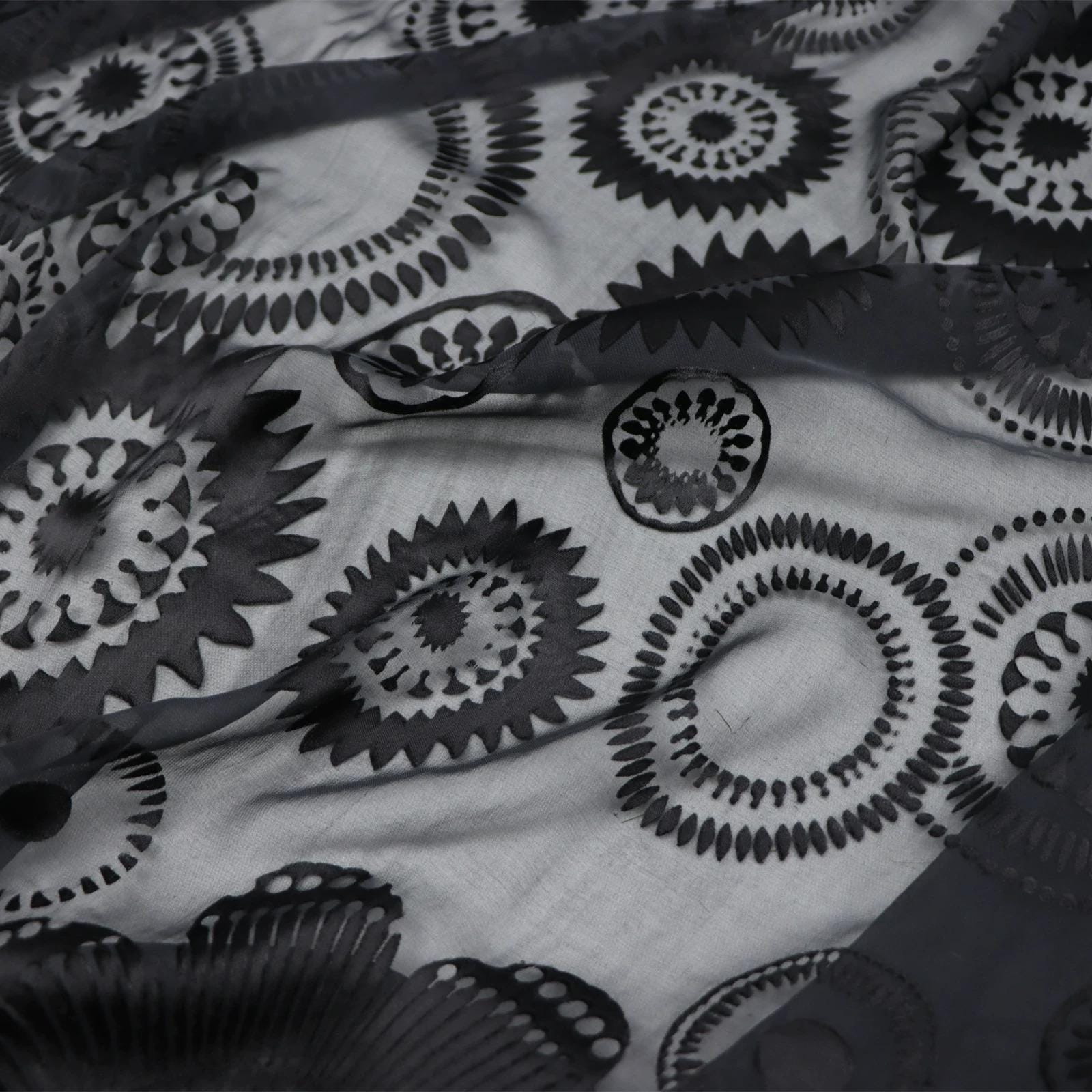 The image is a close-up view of a black and white fabric with a repeating pattern of circular designs. The pattern consists of various sizes and orientations of circles, creating a visually striking and intricate design.