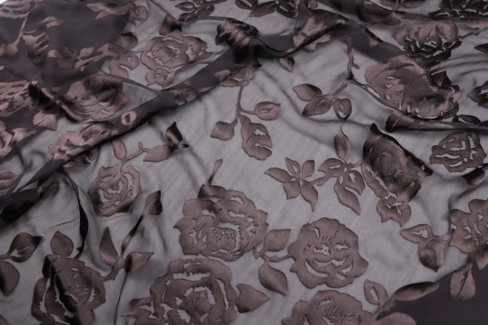 a close-up view of a fabric with a floral pattern, featuring a repeating design of brown roses and leaves.
