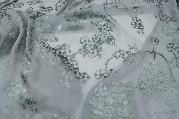 a close-up view of a fabric with a floral pattern, featuring a mix of white and gray colors.