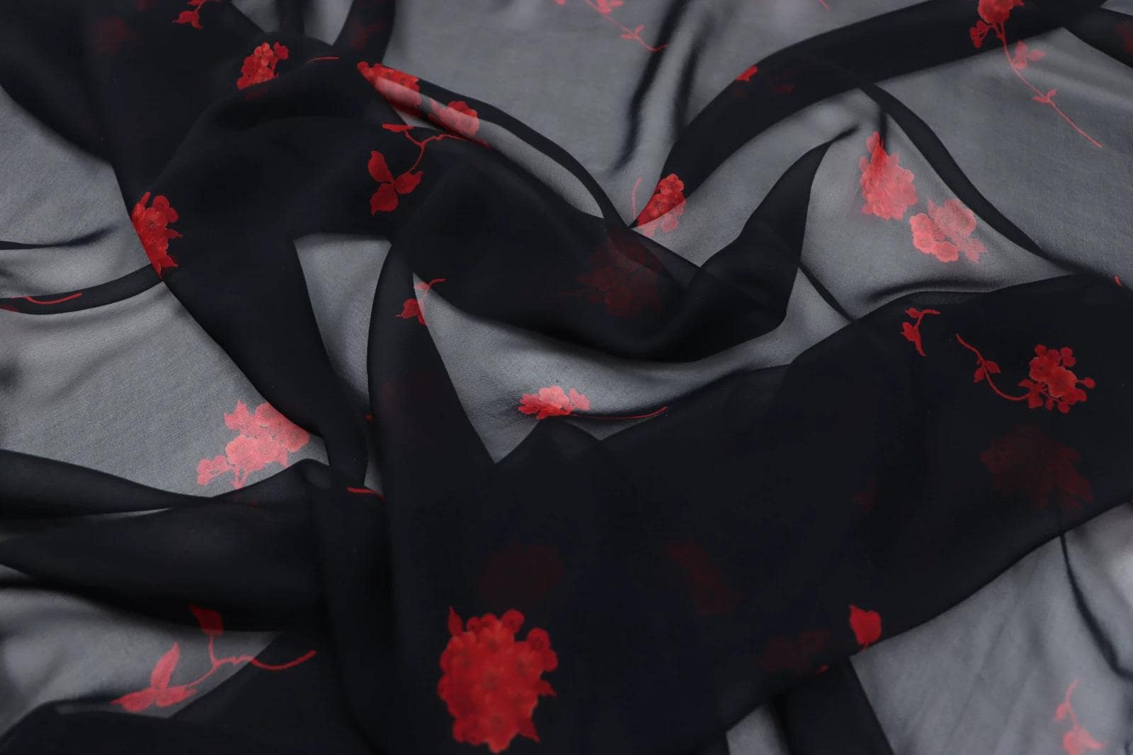 a close-up view of a fabric with a black and red floral pattern. The fabric appears to be made of silk or chiffon, and the pattern consists of red flowers against a black background. The fabric is crumpled and wrinkled, giving it a textured and soft appearance.
