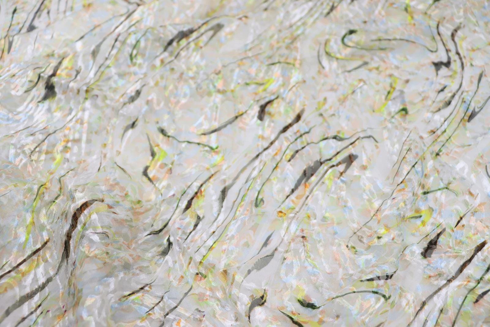 The image is a close-up of a fabric with a textured, abstract pattern of lines and shapes in various colors, including shades of green, yellow, and white.