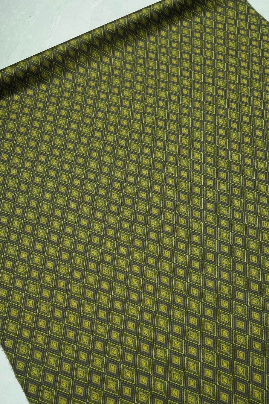 a close-up view of a fabric with a repeating diamond pattern in shades of green and black. The pattern is composed of small squares arranged in a diagonal grid, creating a visually striking and intricate design.