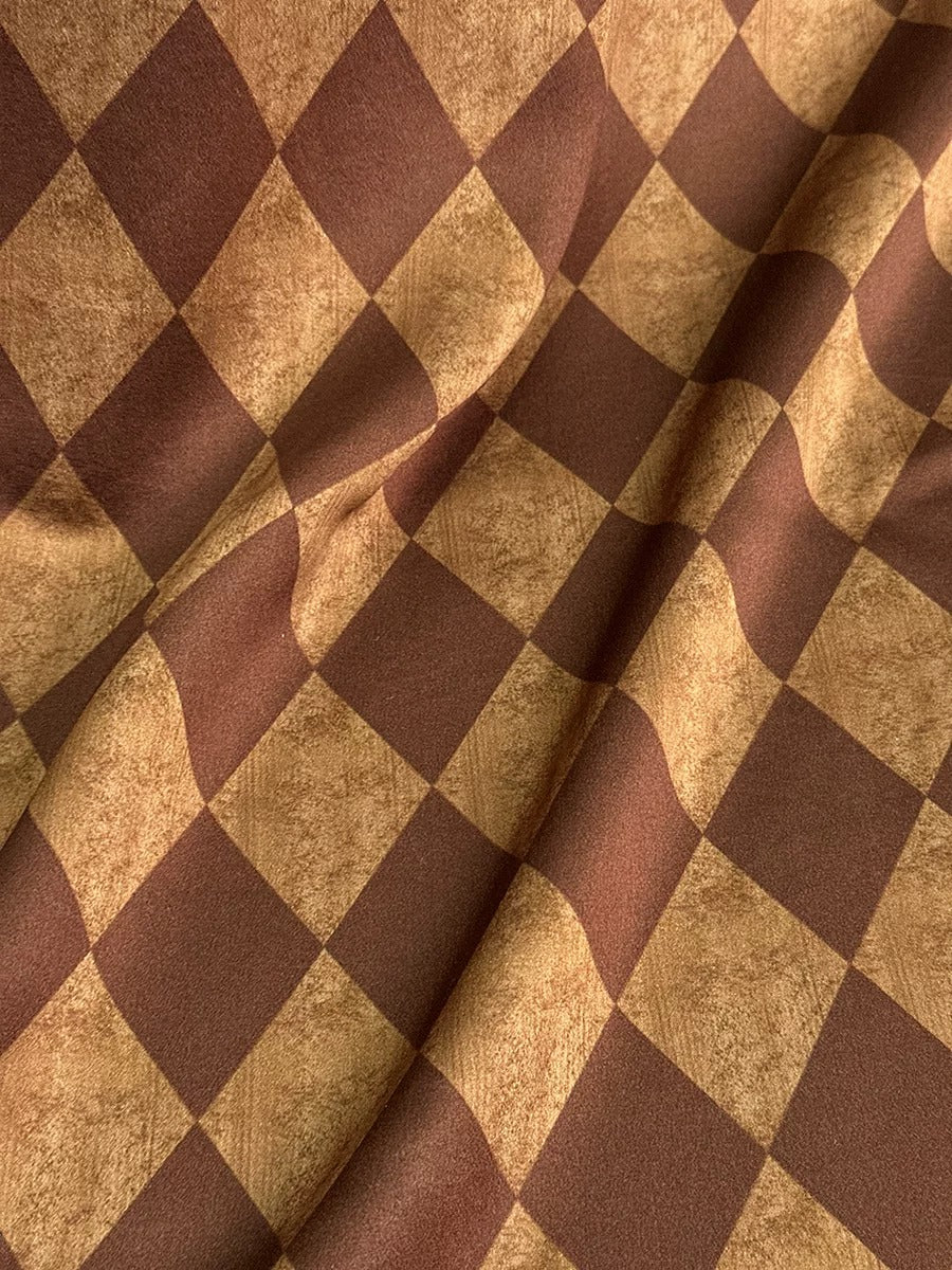 a close-up view of a fabric with a checkered pattern in shades of brown and tan. The fabric appears to be made of a soft, textured material, possibly cotton or a similar type of textile. The pattern consists of a series of small squares or rectangles arranged in a diagonal pattern, creating a visually interesting and textured appearance.