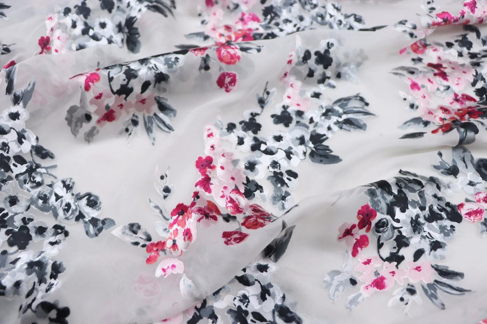 a close-up view of a fabric with a floral pattern in shades of pink, black, and white. The pattern appears to be a mix of different flowers and leaves, creating a visually appealing and intricate design.
