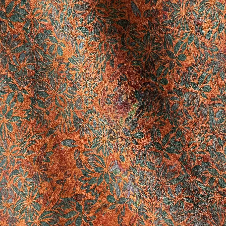 a close-up view of a fabric with a vibrant, intricate floral pattern in shades of orange, green, and blue. The pattern is composed of numerous small flowers and leaves, creating a visually striking and detailed design.