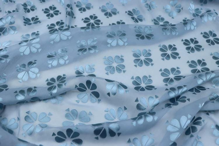 a close-up view of a fabric with a repeating pattern of blue and white flowers. The fabric appears to be made of a soft, flowing material, and the pattern is quite intricate and detailed.