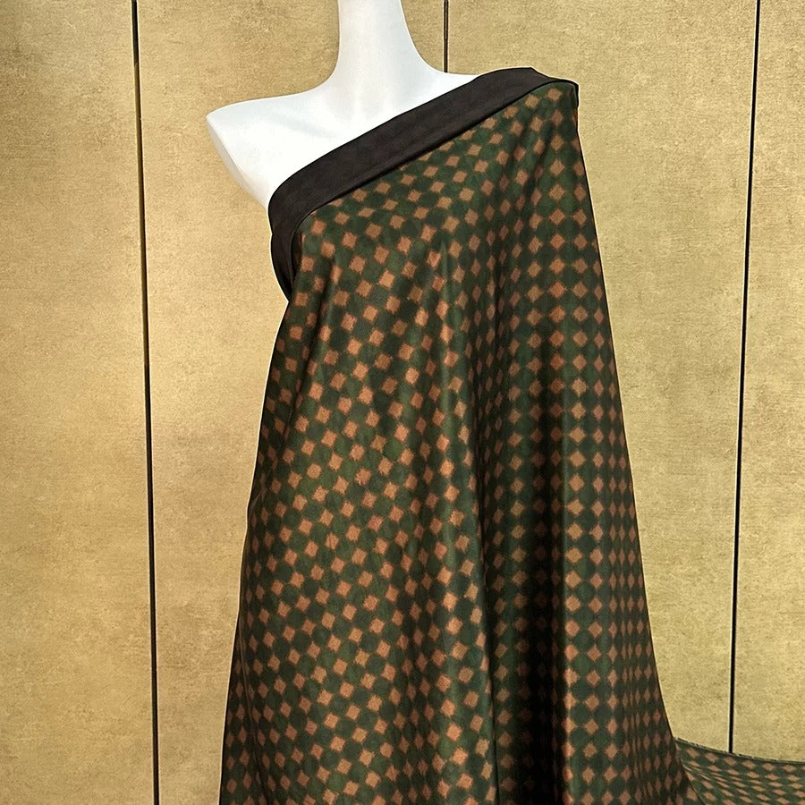 A mannequin wearing a green and brown patterned fabric draped over its body.