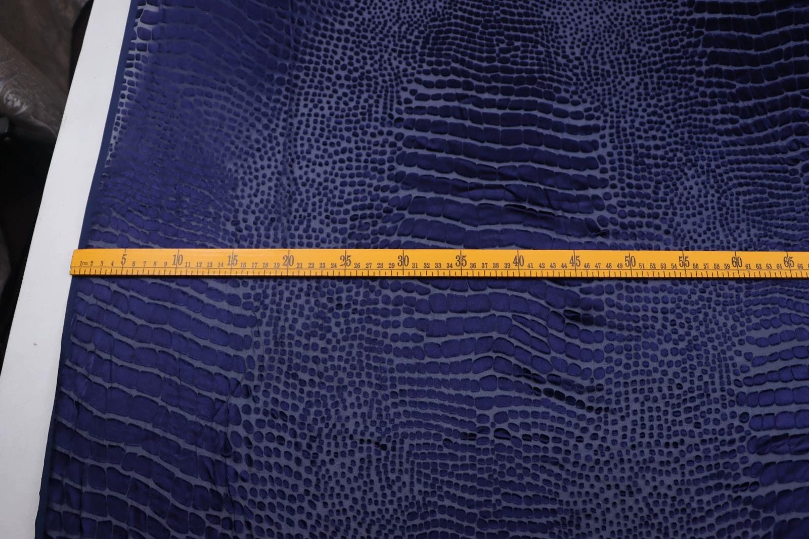 a close-up view of a blue fabric with a textured pattern, featuring a yellow measuring tape placed across it.