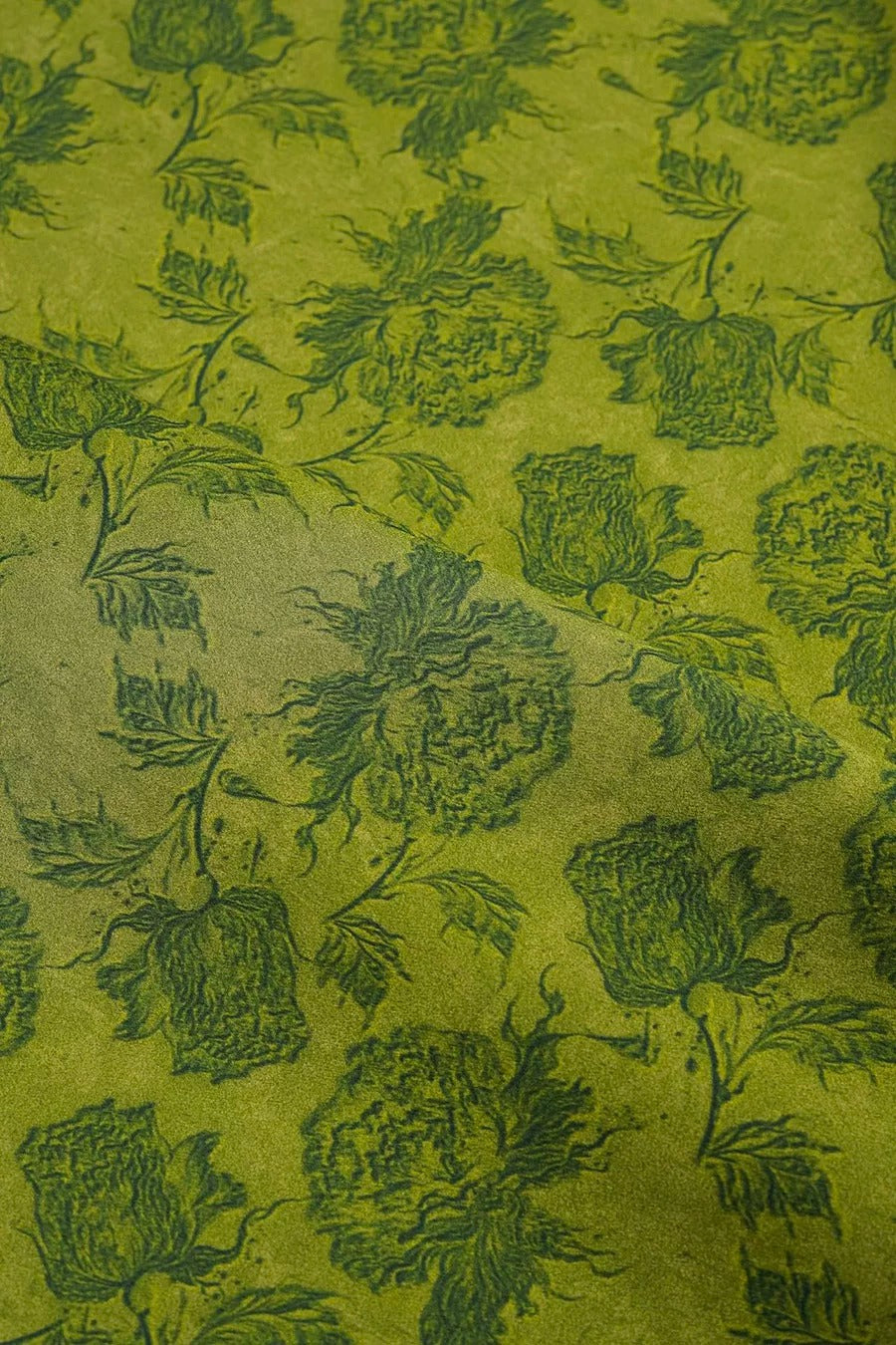 a close-up view of a fabric with a repeating pattern of green floral designs. The pattern consists of various flower shapes and leaves, creating a visually striking and intricate design. The fabric appears to be a type of wallpaper or textile, with the green color and floral pattern suggesting it could be used for decorative purposes or as a design element in interior spaces.