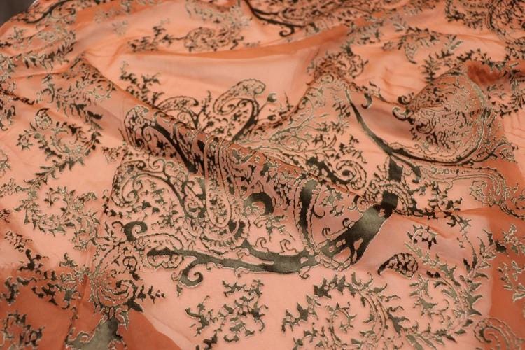a close-up view of a fabric with a detailed, intricate paisley pattern in shades of orange and black.