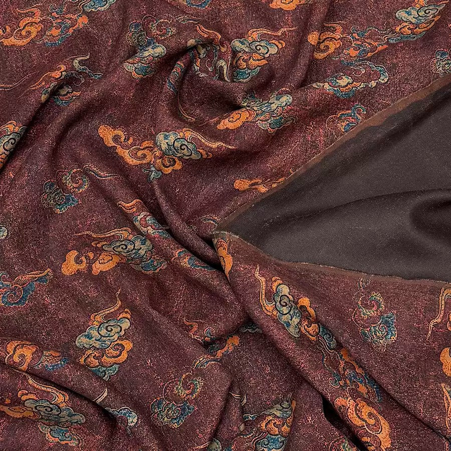 a close-up view of a fabric with a maroon color and a pattern of clouds and swirls in various shades of orange and blue.