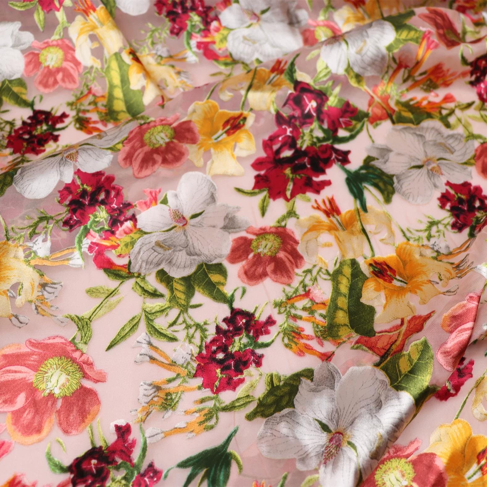 The image is a close-up view of a fabric with a vibrant floral pattern. The fabric is adorned with a variety of colorful flowers, including red, yellow, and white flowers, as well as green leaves. The flowers are intricately embroidered, adding a detailed and textured appearance to the fabric. The overall composition of the image is visually appealing and showcases the beauty of the floral pattern.