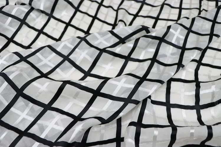 a close-up view of a fabric with a black and white checkered pattern. The fabric appears to be made of a sheer material, with a grid-like design consisting of black and white squares. The fabric is crumpled, giving it a textured appearance.