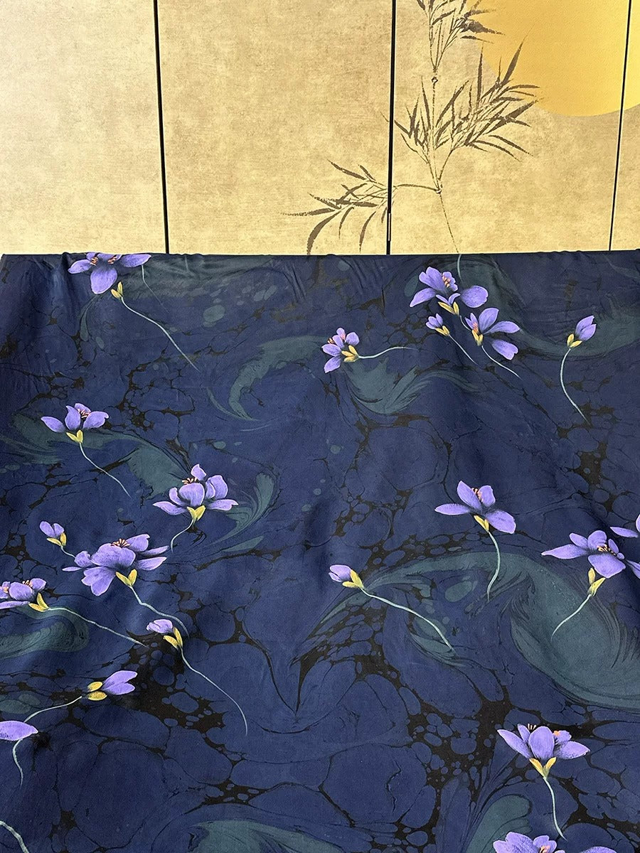 a dark blue fabric with a floral pattern of purple flowers and green leaves. The fabric appears to be a piece of clothing or textile, with the floral design prominently displayed.