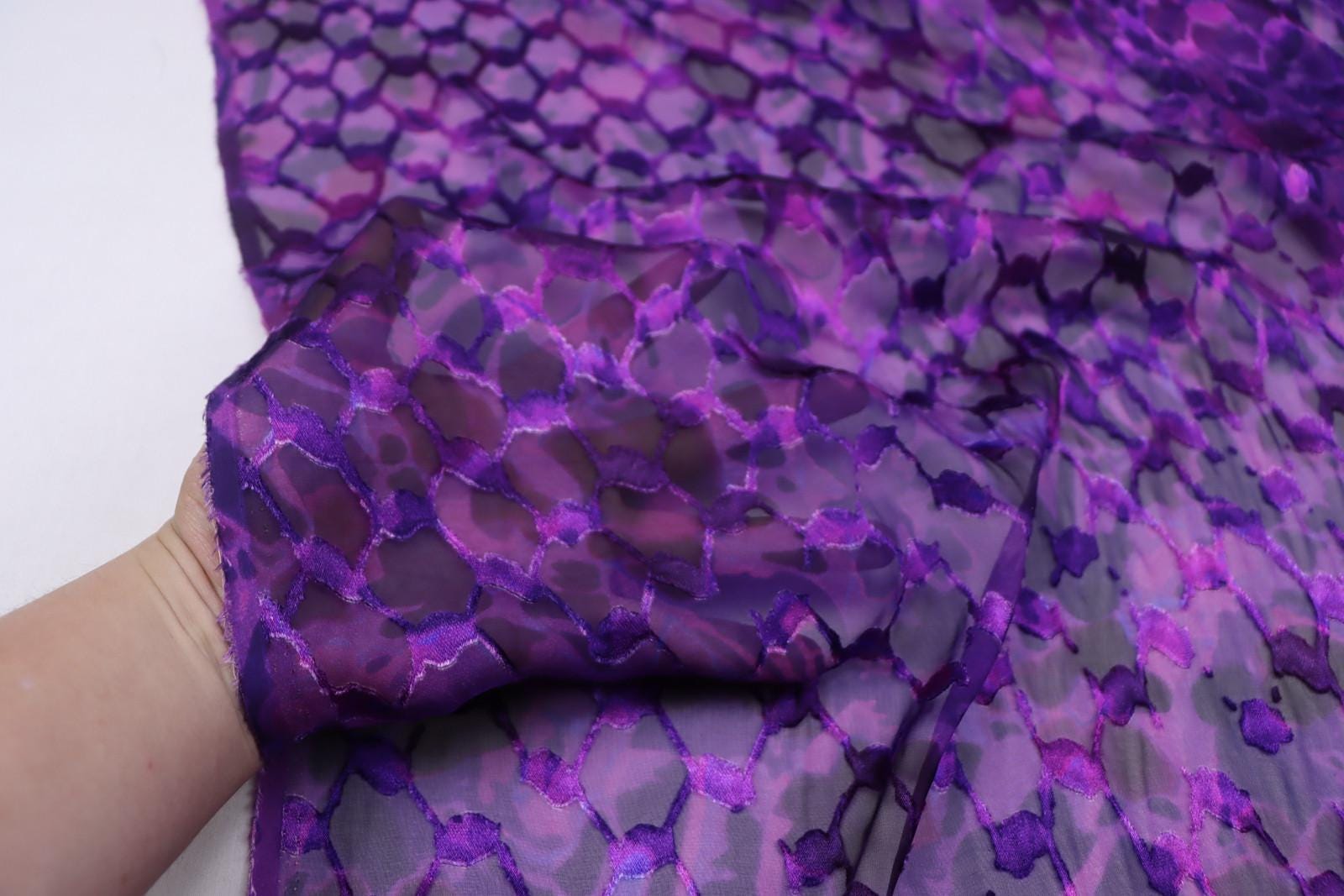 A close-up view of a hand holding a piece of fabric with a purple and black patterned design.