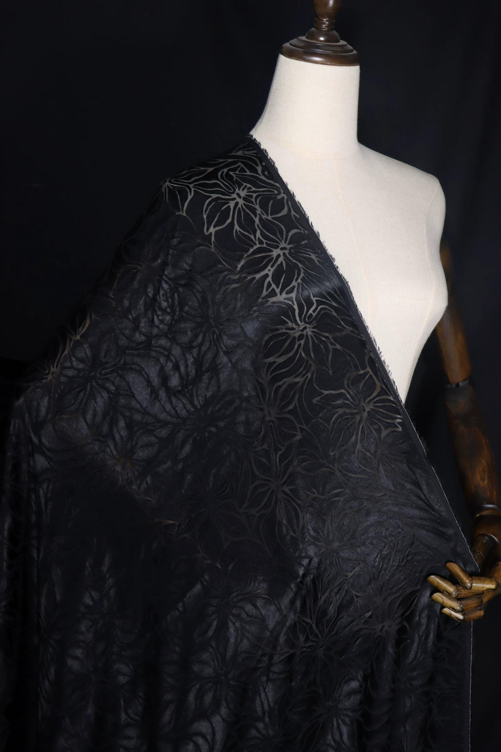 A mannequin wearing a black fabric with a floral pattern, displayed against a dark background.