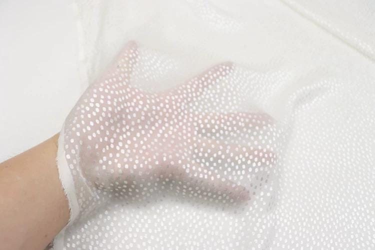 A hand is holding a white fabric with small white dots on it.