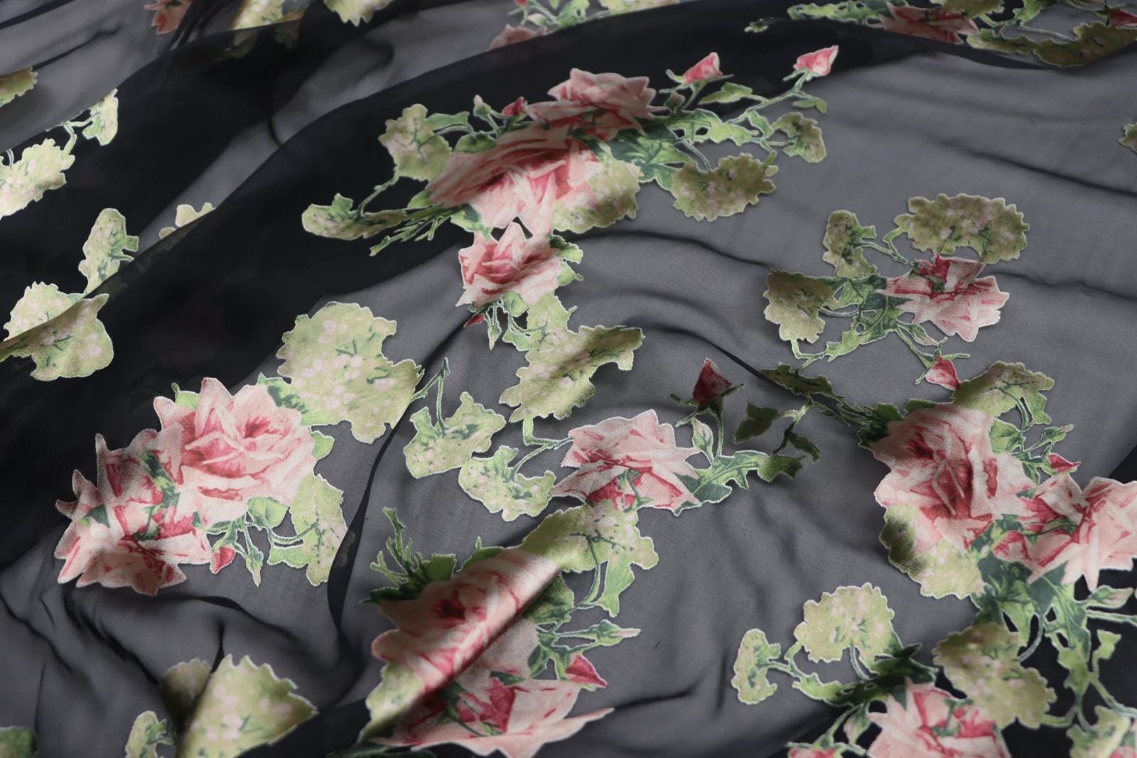 a close-up view of a fabric with a floral pattern, featuring pink and green flowers against a dark background.