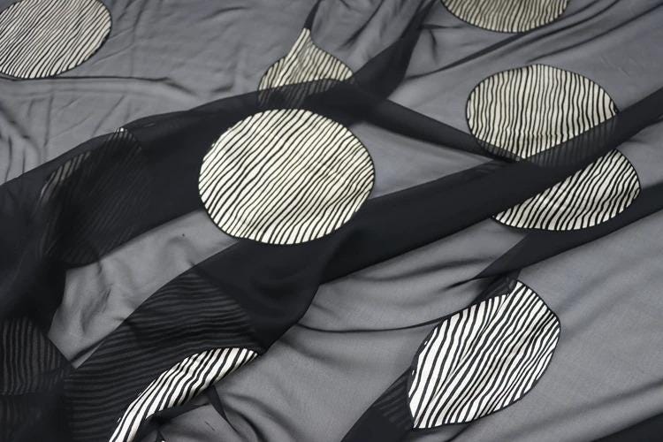 a close-up view of a fabric with a repeating pattern of circular shapes in black and white. The pattern consists of several circles of varying sizes, creating a visually striking and textured design.