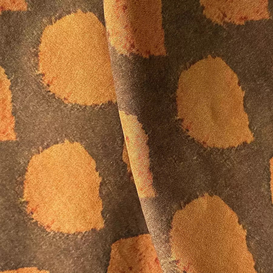 a close-up view of a fabric with a repeating pattern of orange circles or spots on a dark background.