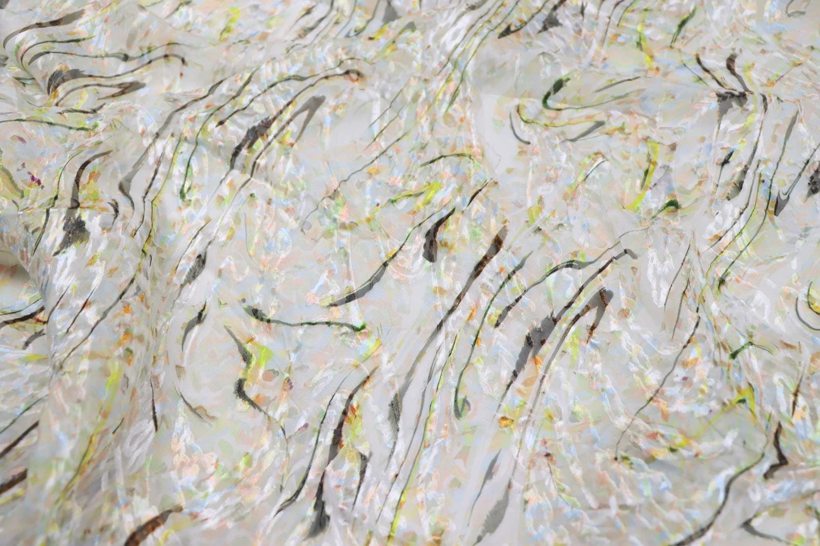 The image is a close-up of a fabric with a marbled pattern, featuring a mix of white, black, and yellow colors.
