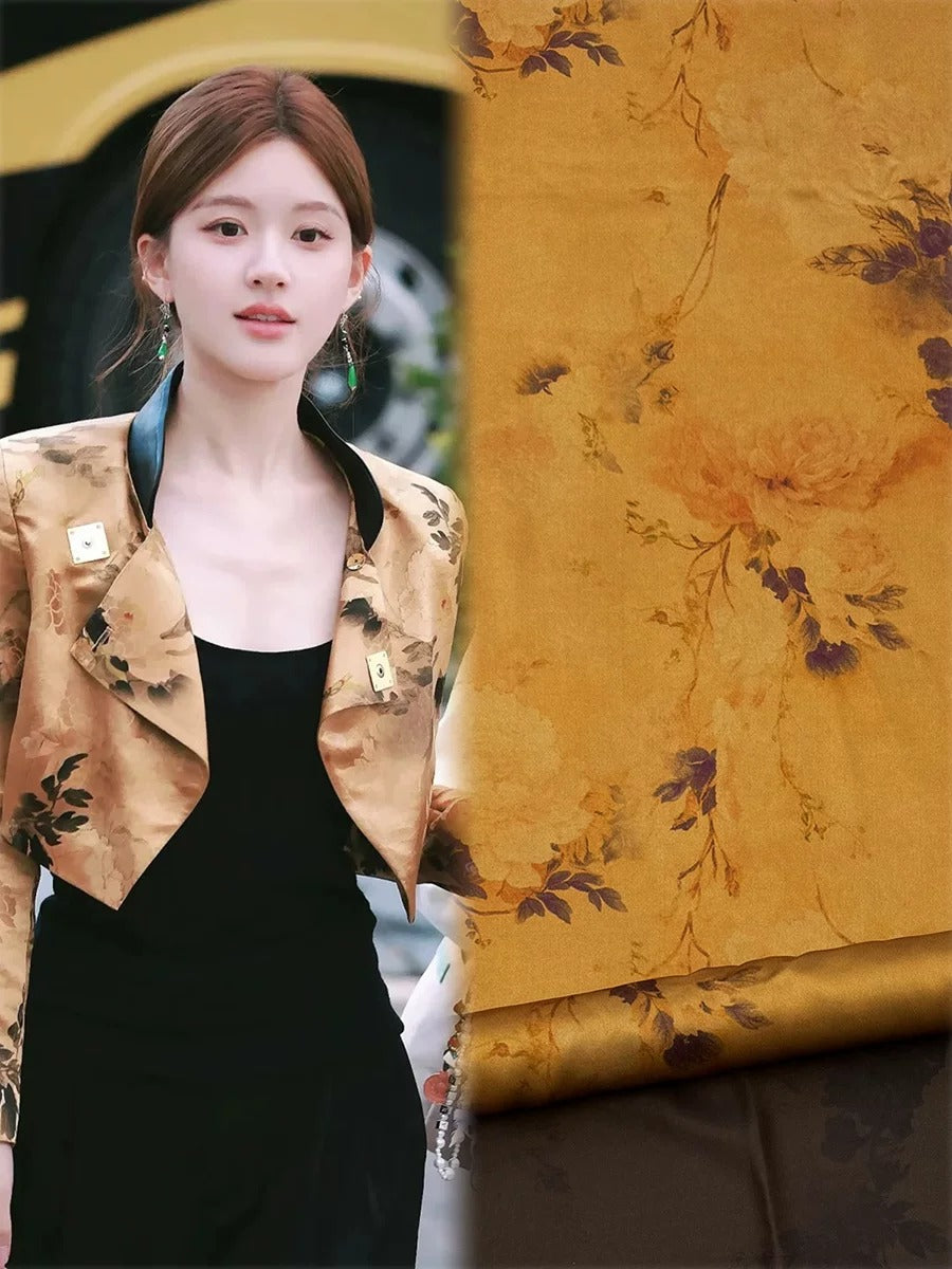 A woman wearing a gold floral print jacket and black dress stands in front of a fabric with a floral pattern.