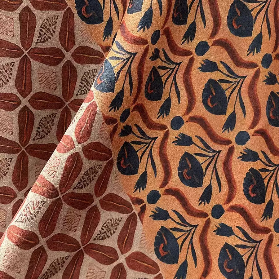 a close-up view of a fabric with a repeating pattern of floral and leaf designs in shades of orange and black.