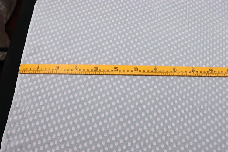 a yellow ruler placed on a white fabric with a pattern of white polka dots.