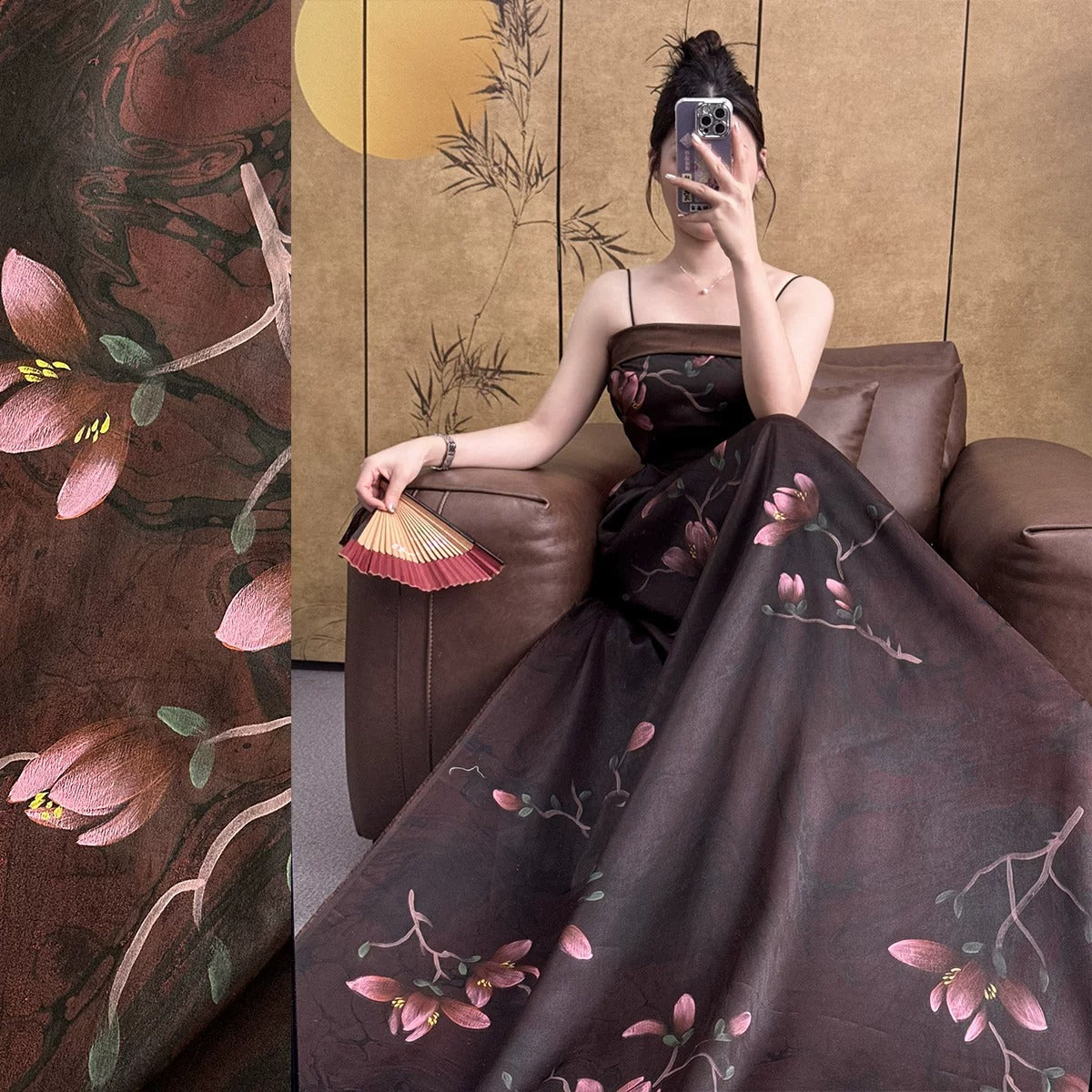 A woman in a long, dark dress with floral patterns is sitting on a couch, holding a fan and taking a selfie with her phone.