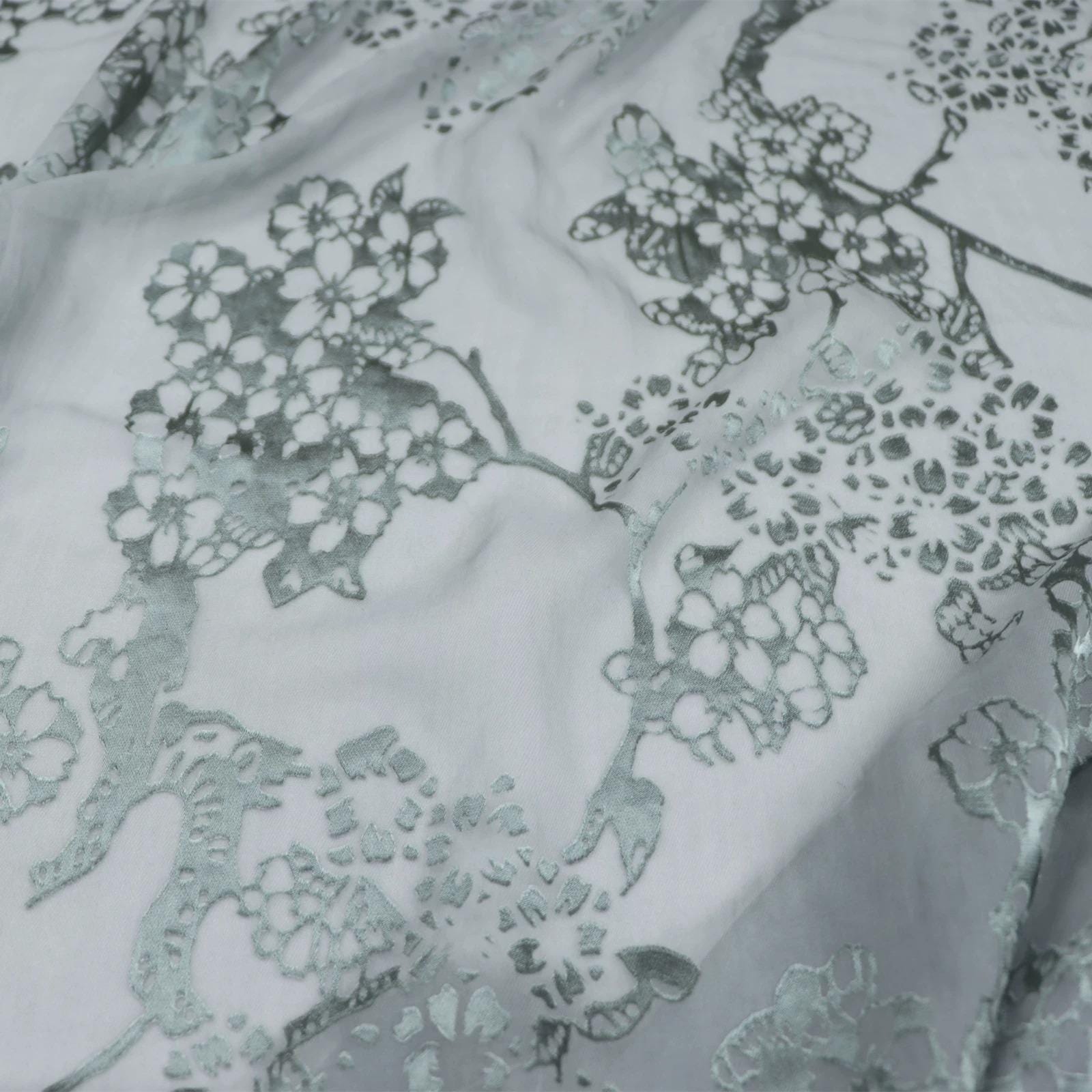 a close-up view of a fabric with a floral pattern, featuring a repeating design of white flowers against a light gray background.