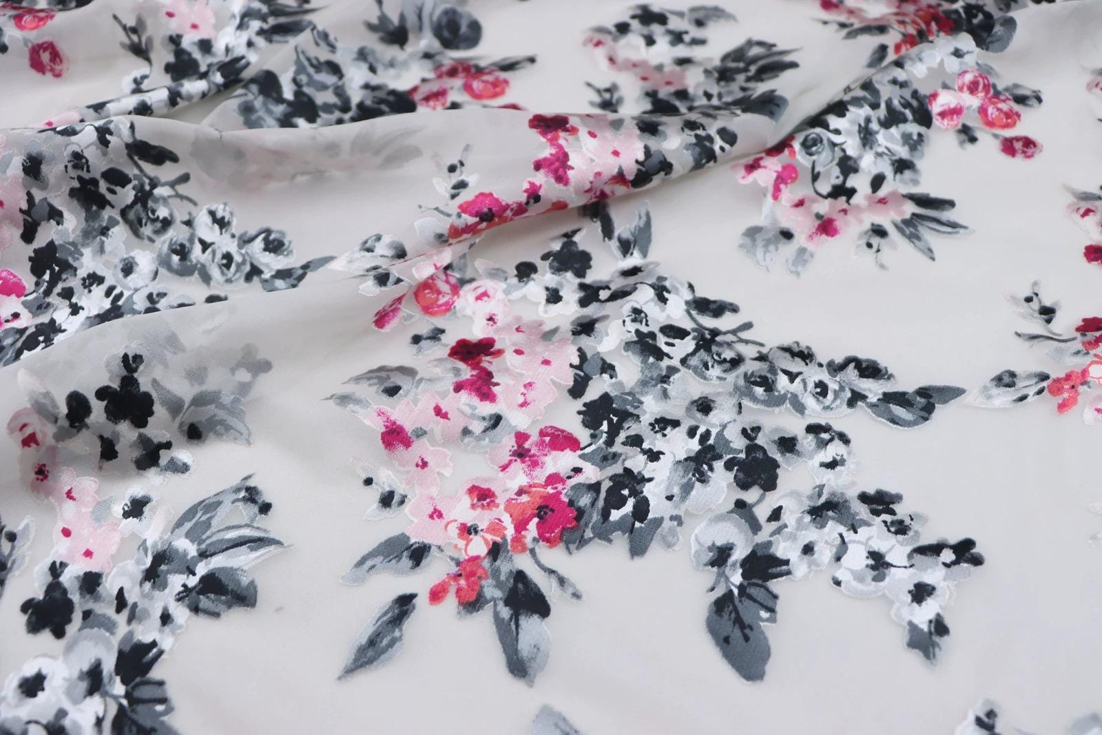 a close-up view of a fabric with a floral pattern in shades of pink, black, and white. The pattern appears to be a mix of flowers and leaves, creating a visually appealing and intricate design.