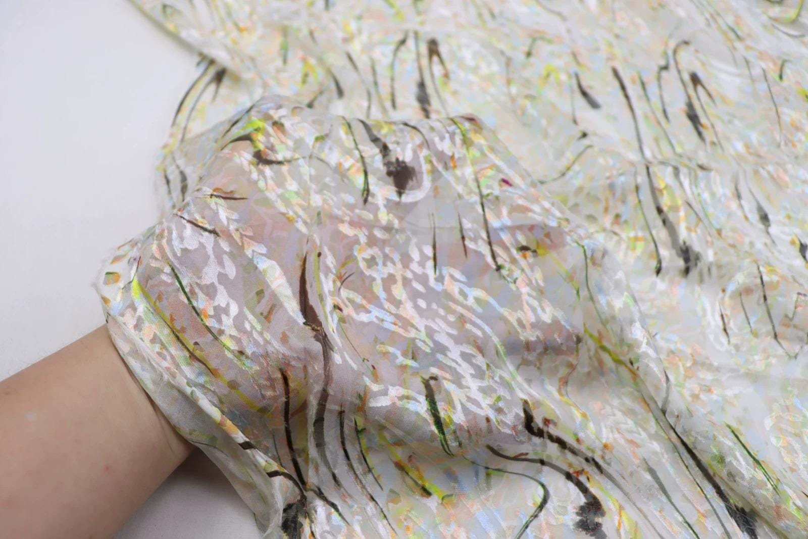 a close-up view of a hand holding a piece of fabric with a colorful, abstract pattern.