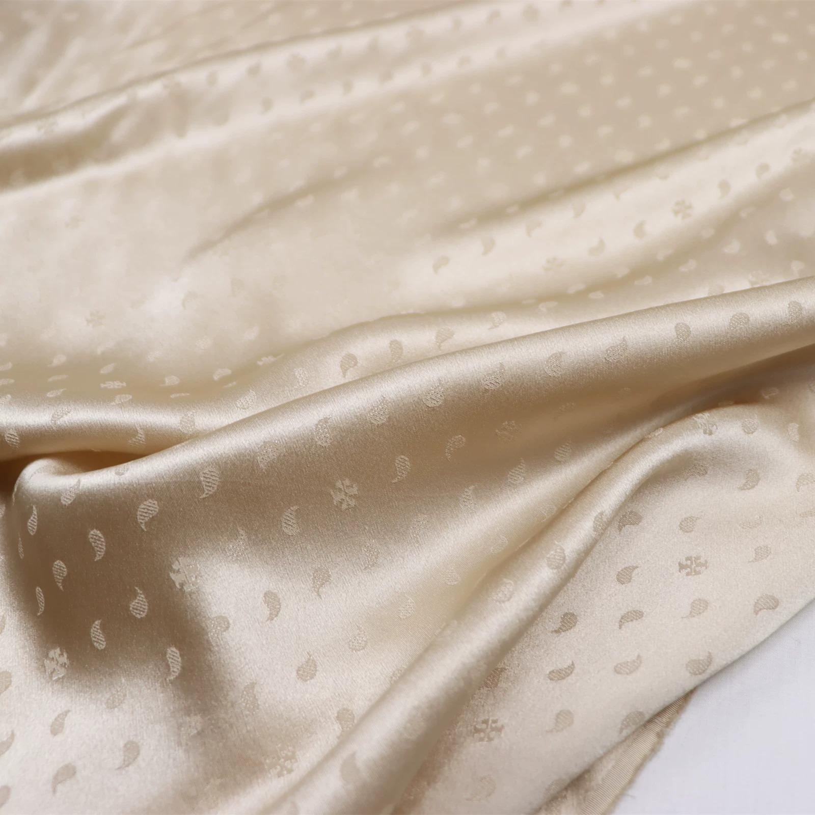 a close-up view of a fabric with a repeating pattern of small white dots or circles, creating a textured and shiny appearance.